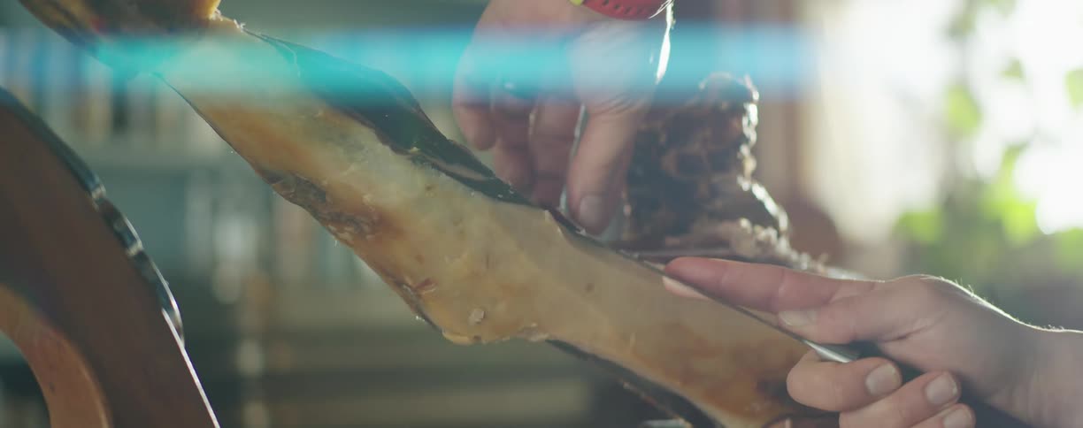 A man carves thin slices of cured ham from a whole leg