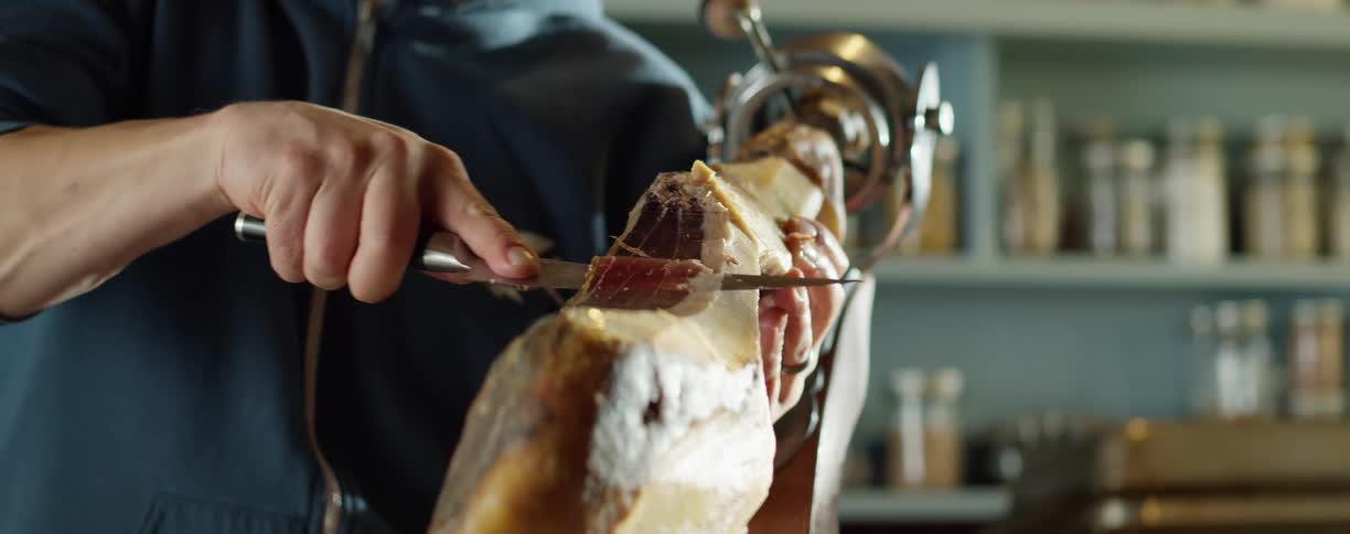 Man uses a sharp knife to slice a piece of serrano spanish ham