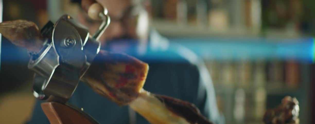 Man uses a sharp knife to cut a slice of spanish serrano ham