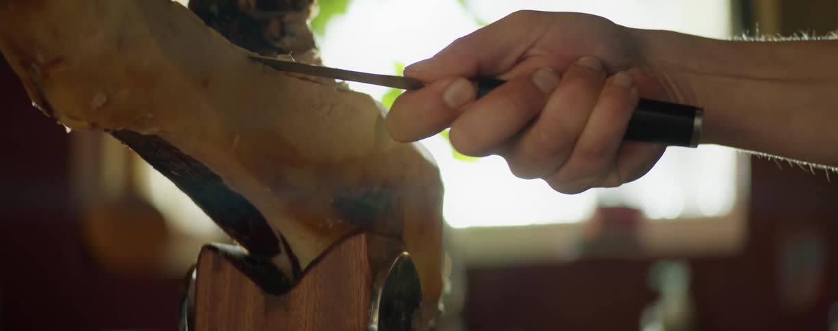 A man thinly slices meat from the leg of a roasted pig