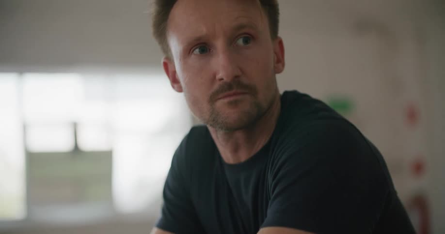 A man rests his arms on the handle of a floor sander as he looks around casually