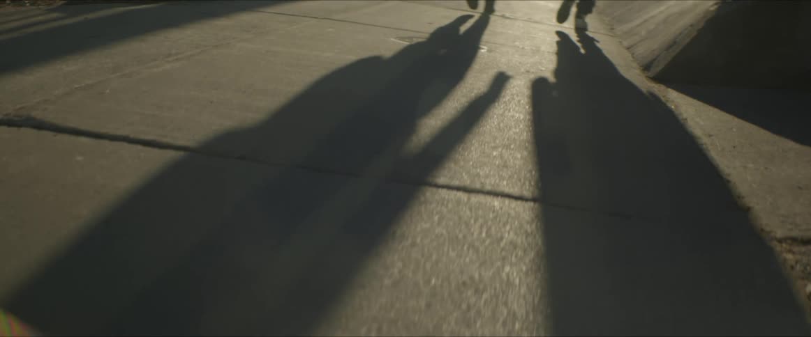 The shadows of two young men are reflected on the sidewalk as they walk past a mound of snow
