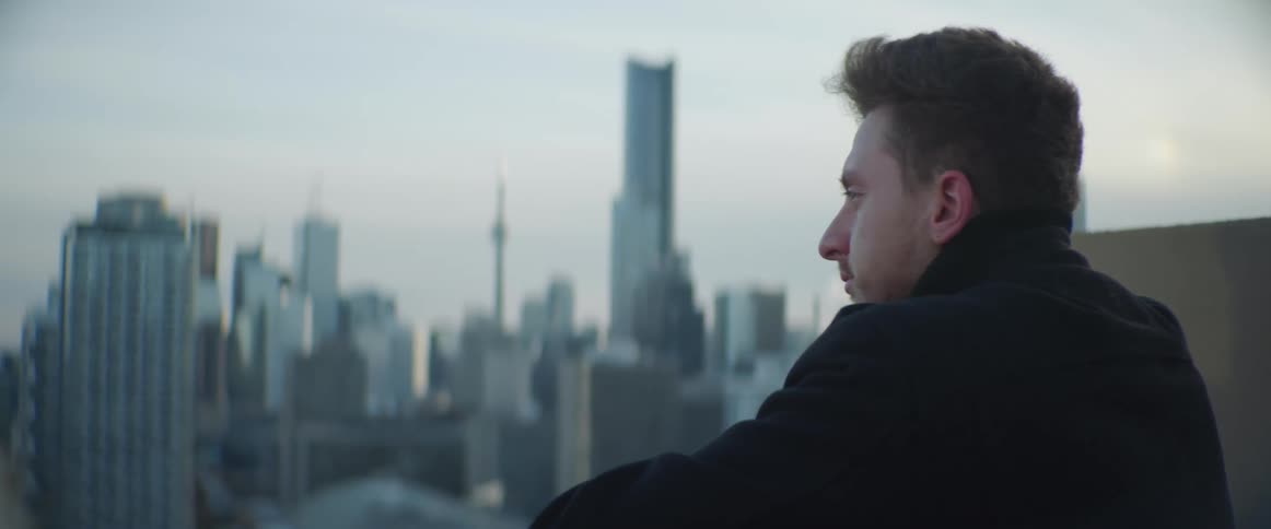 A man on a rooftop with the city skyline the sky and clouds in the background