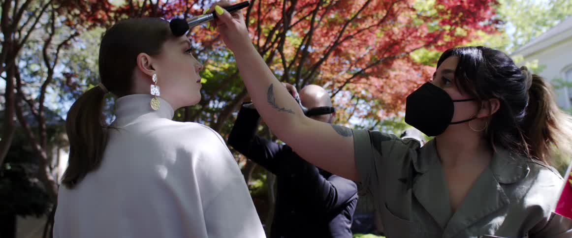 Makeup artist touches up models makeup as photographer holds camera up