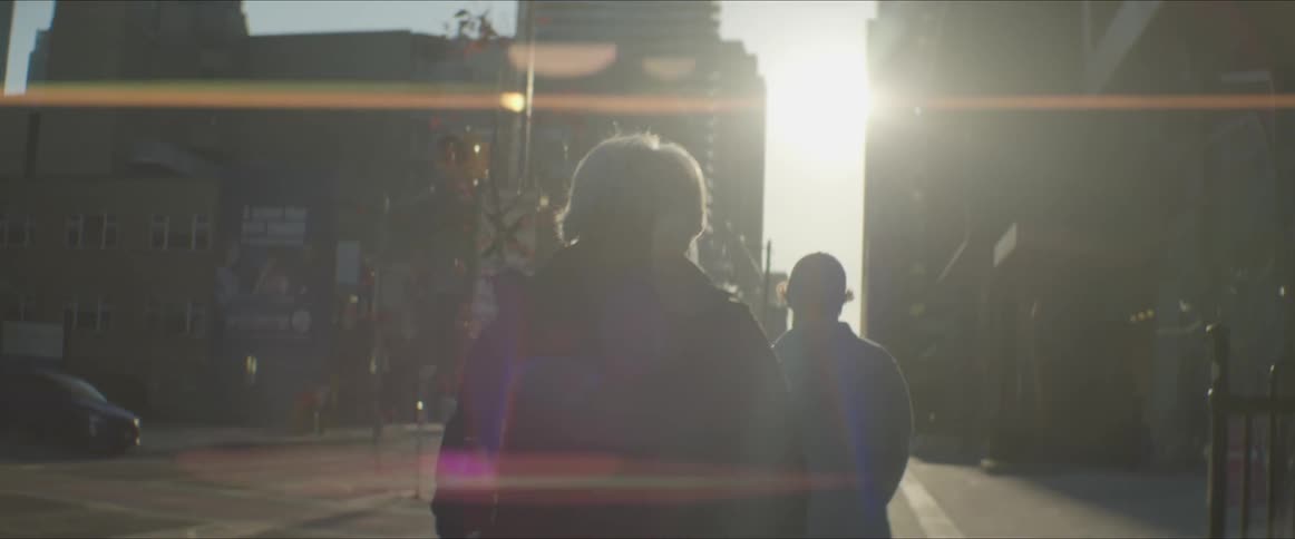 People walking in a city with buildings the sun the sky and clouds in the background