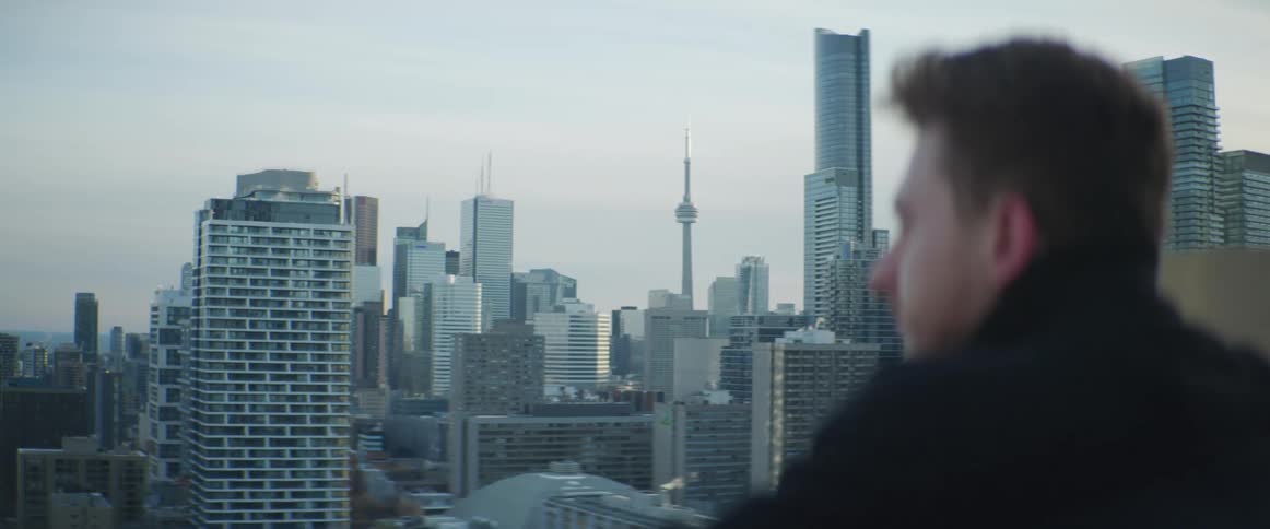 A man standing on a rooftop overlooking a city with high rise buildings at sunrise