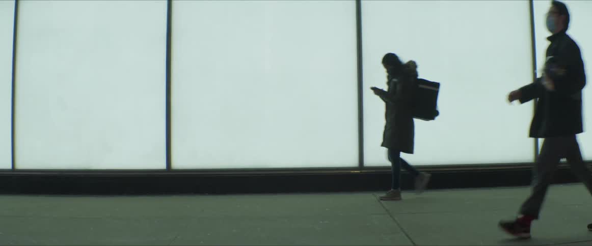 Pedestrians walking by on a sidewalk in a city in front of a light display at night