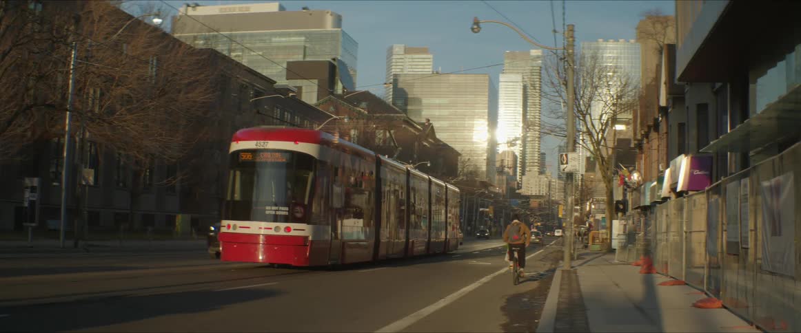 A city street with a trolley with buildings the sky and clouds in the background