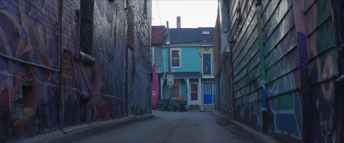 An alleyway with graffiti with houses the sky and clouds in the background