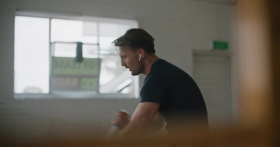 A middle aged man sings into the handle of a mop while listening to music through his ear buds while mopping the floor