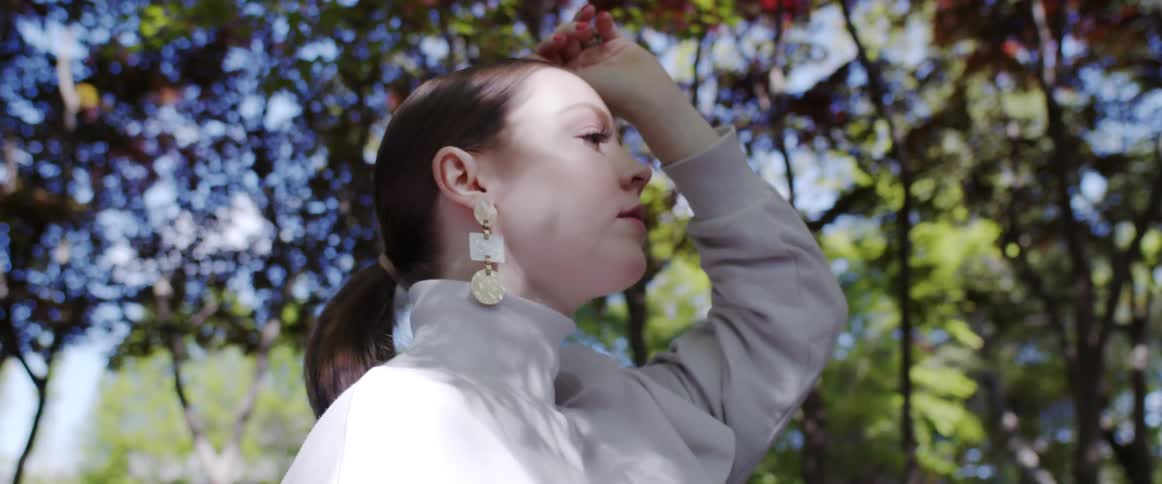 Young pale woman modeling for a camera under the trees outdoors