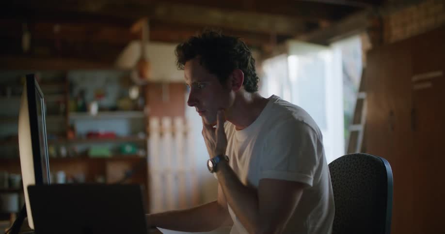 A man sitting at a desk working on a computer inside of a garage at daytime