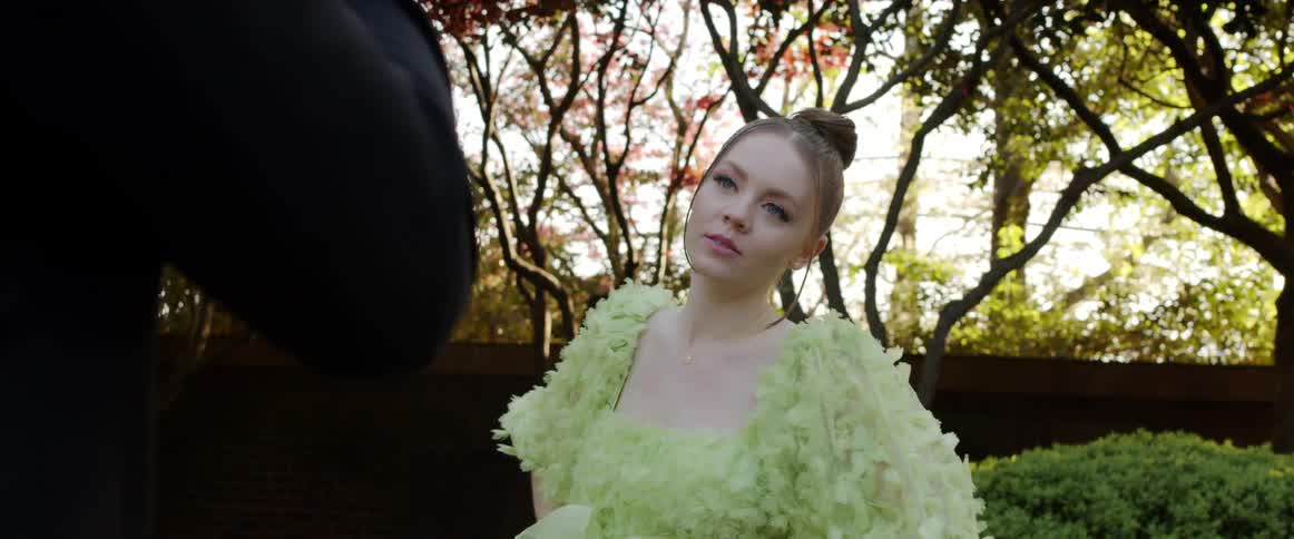 A model in a yellow gown poses in a yard with trees and bushes behind her