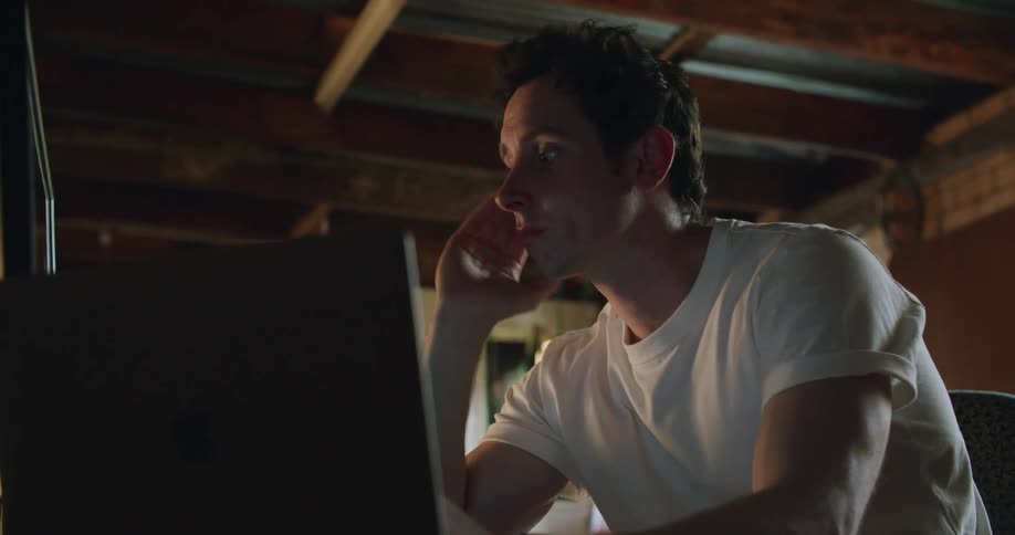 A man types on a computer with one hand while sitting at a desk