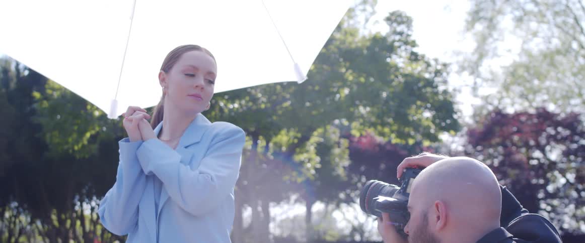 A model in a pale blue pantsuit poses with her hands clenched together as a photographer takes her picture