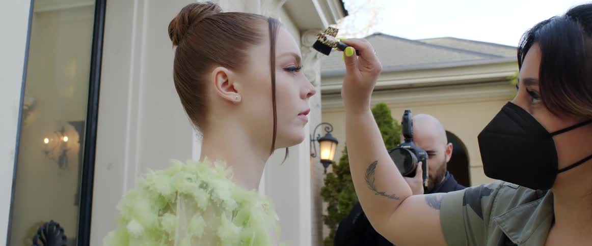Female model stands still while someone retouches her makeup during a photoshoot
