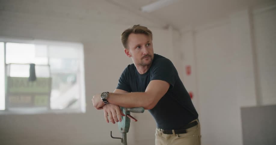 A man with a wristwatch in a room with a wall and window in the background