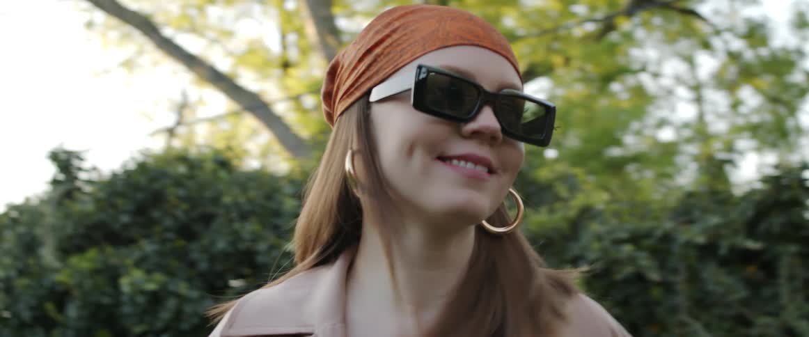 Woman wearing sunglasses and a headband modeling for a camera outdoors