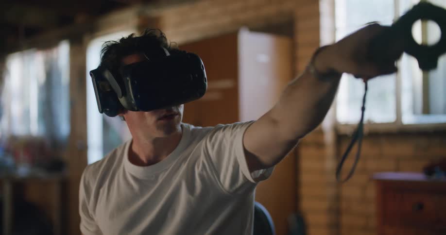 A man wearing vr headset goggles and holding a black remote moving his arm around