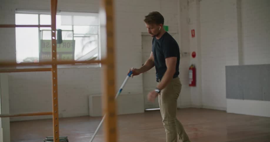 Young man cleaning the floor of an empty room with a mop