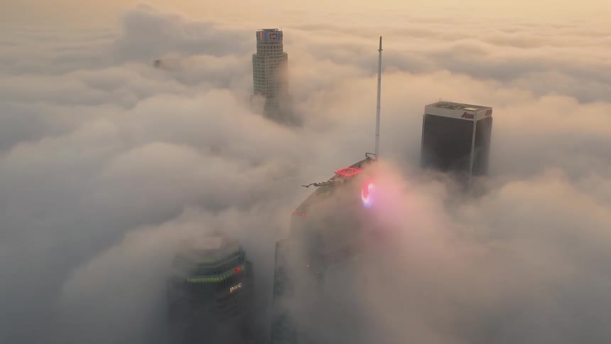 Fog flow over skyscrapers revealing helicopter pad and neon sign