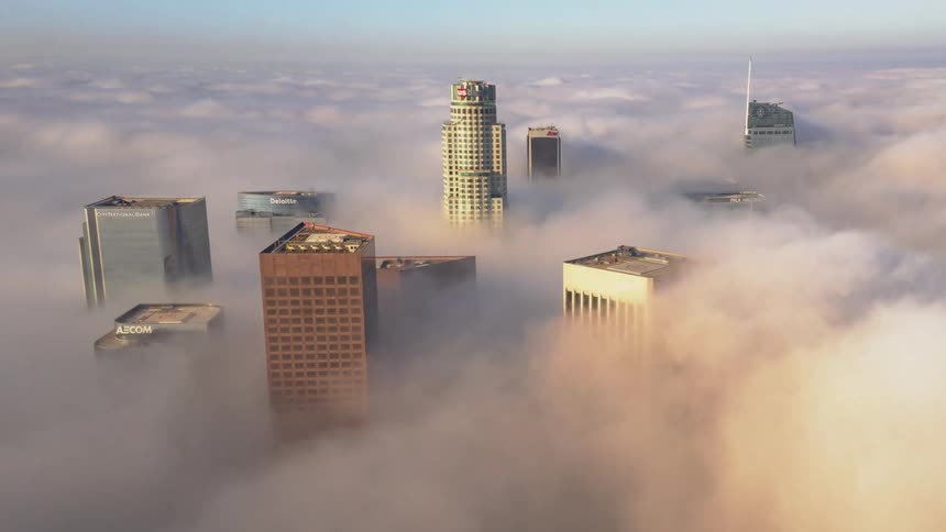 A city skyline with buildings and fog with the sky and clouds in the background