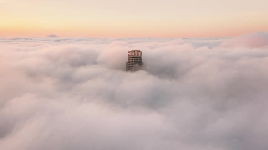 A building surrounded by fog with the sky and clouds in the background