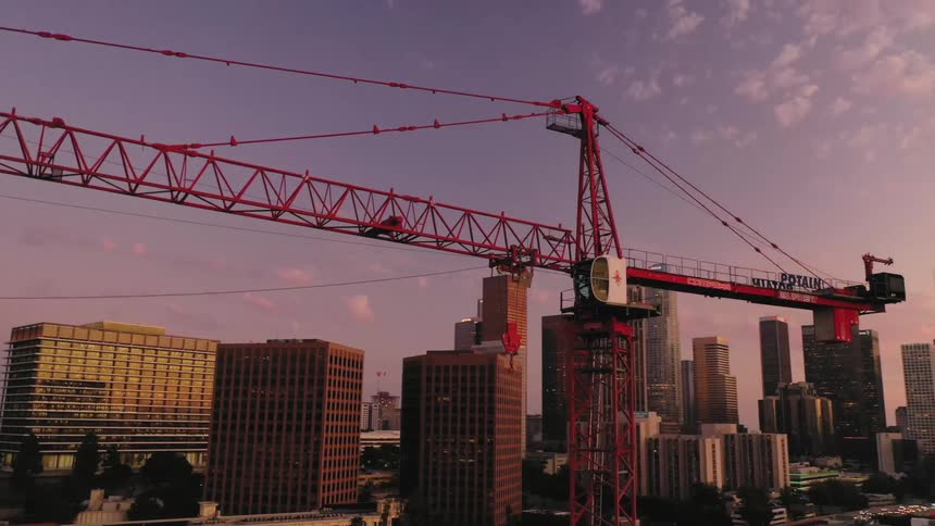 A construction crane with a city with buildings trees and roads the sky and clouds in the background