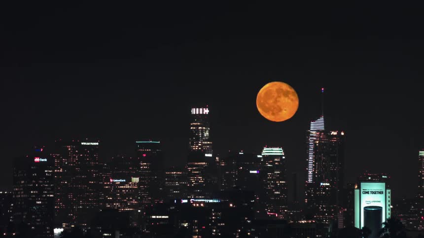The orange full moon rises over a metropolis at night