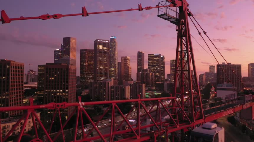 Red construction crane towering in front of the city skyline at sunset