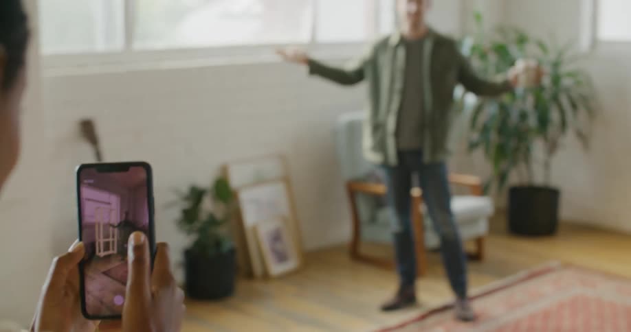 Woman uses mobile phone app to determine shelving unit placement in living room with mans assistance