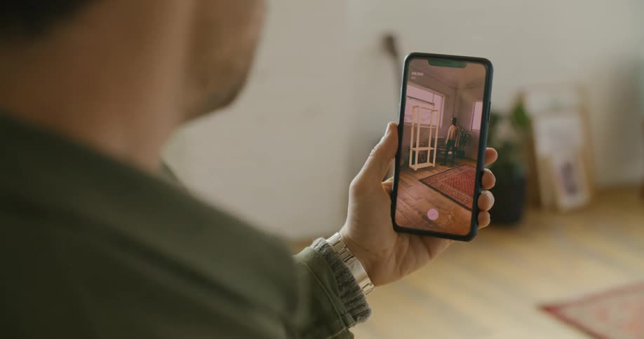 A man taking a picture of a woman on a smartphone while placing virtual furniture on the screen
