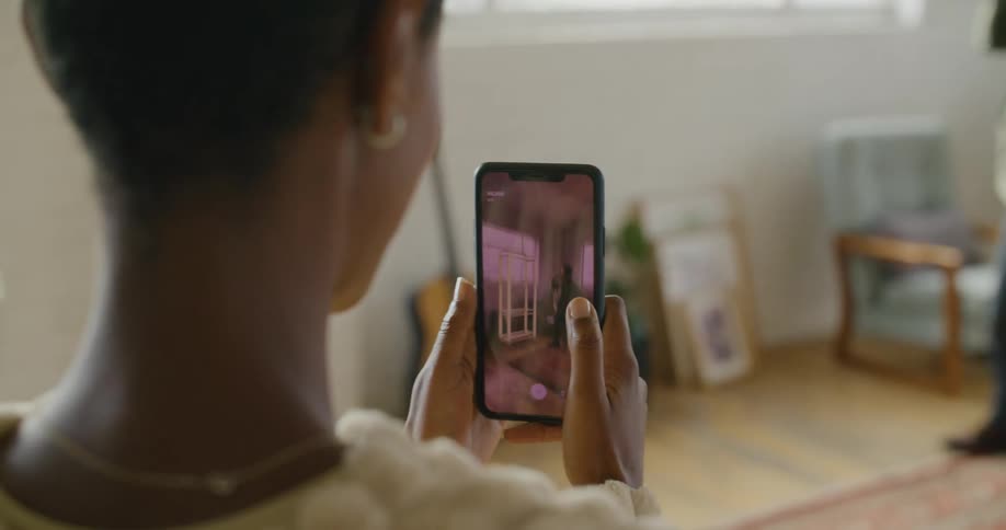 A man stands in a living room while a woman holding a smart phone places a virtual piece of furniture into the room on her screen
