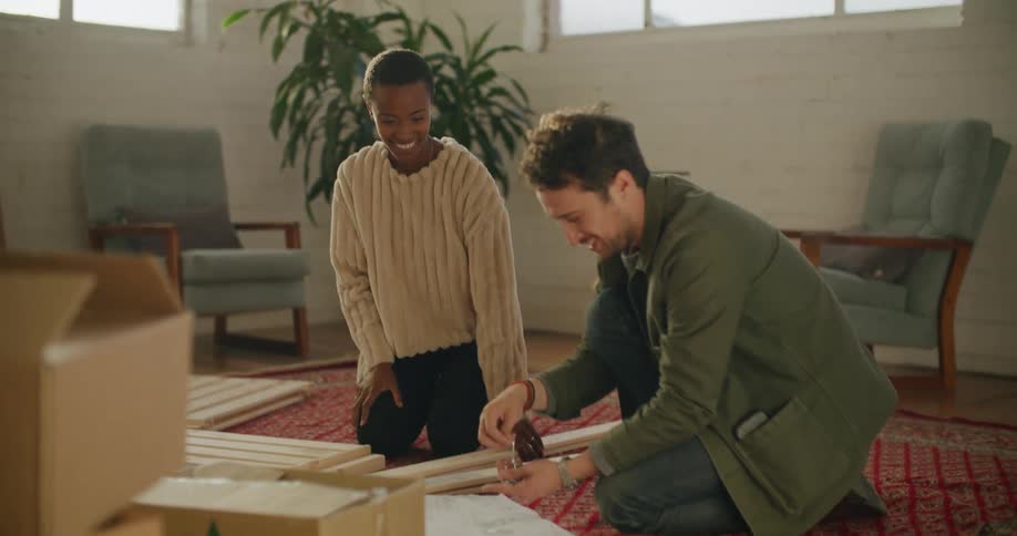Young couple sitting in the living room floor assembling furniture