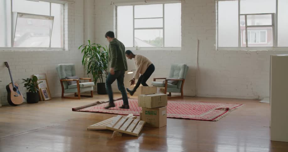 A man and woman unroll an area rug in their new apartment