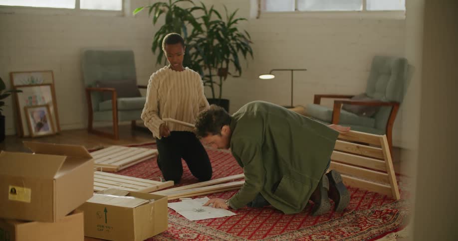 A man and woman assemble furniture while consulting instructions on the floor of the living room of a house during the day