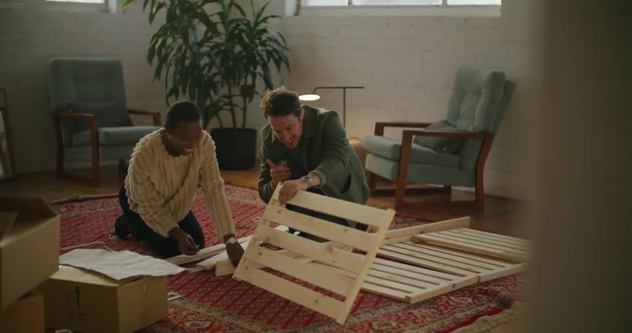 A man and a woman on the floor putting together furniture with a plant and walls in the background