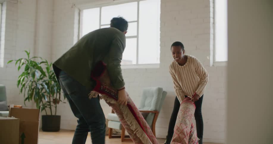 A woman and a man moving a rug into a living room at daytime