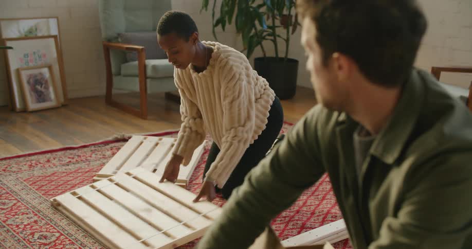 A man and woman unpack boxes and furniture pieces in a living room