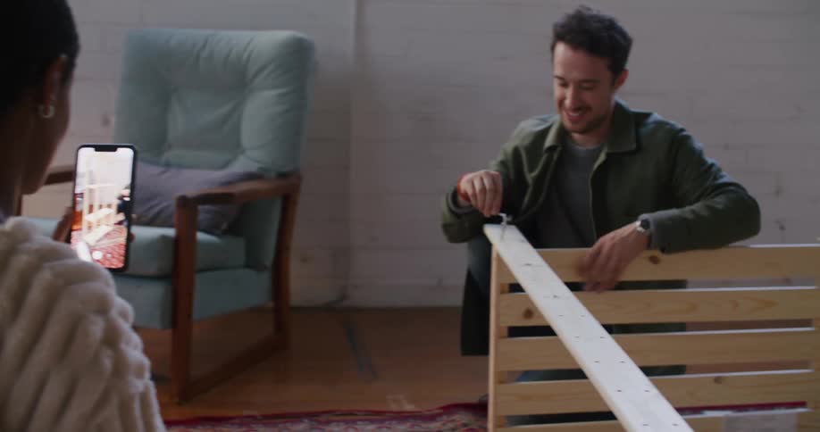 A man tightens a screw with a tool while a woman takes video and talks to him