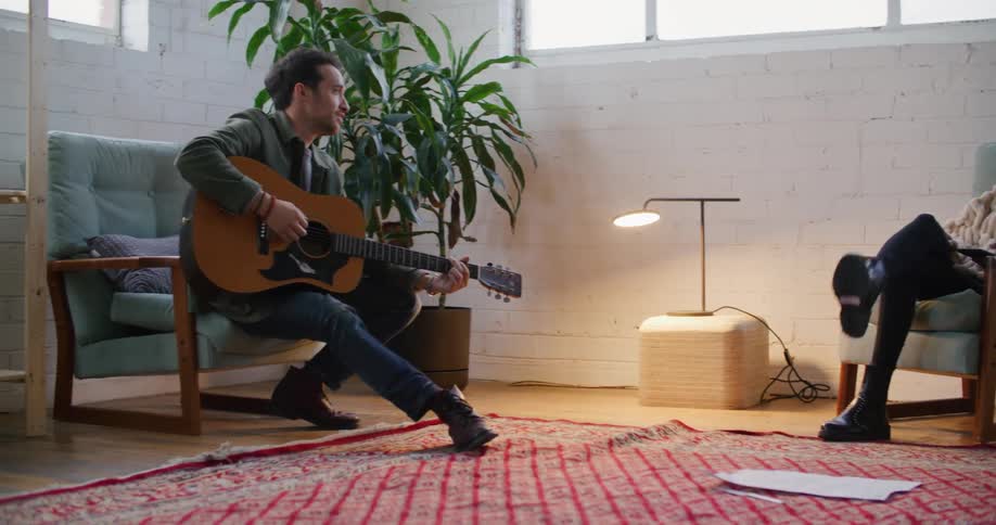Man and woman sitting in living room talk while man plays guitar