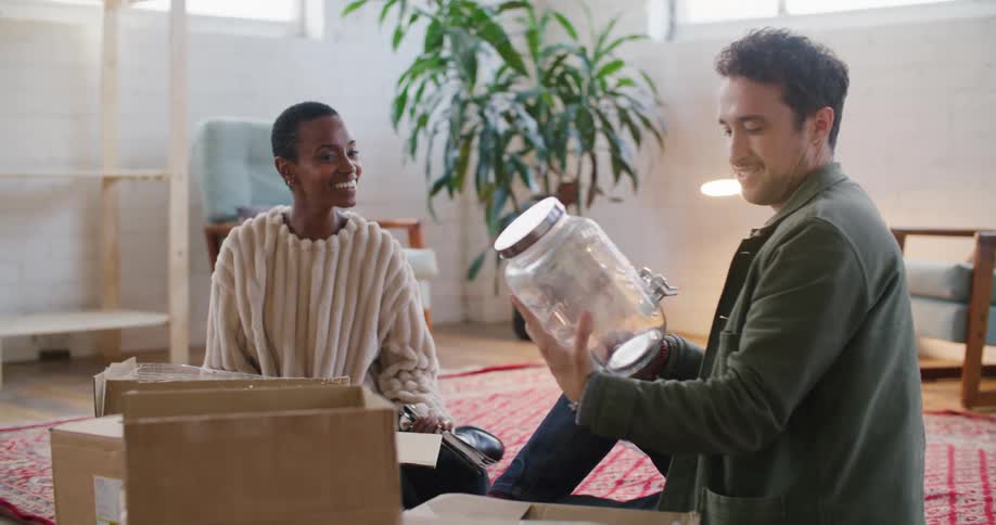Young couple sitting in the living room floor unpacking cardboard boxes