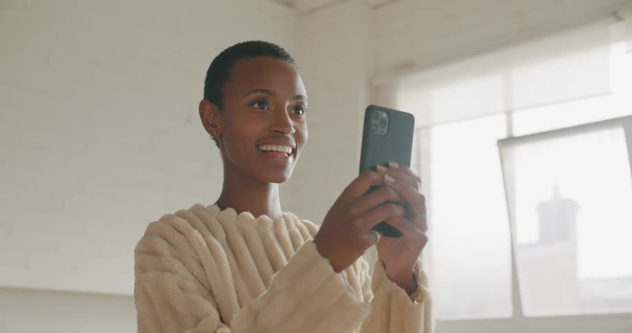 A young woman laughs while taking a photograph with her smartphone indoors during the day