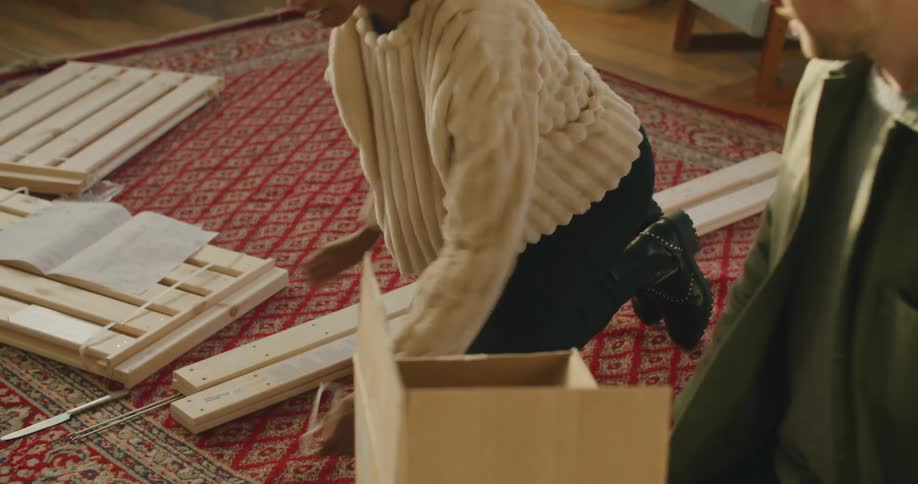 A man and a woman kneeling on a rug in a living room working together to put together a piece of wooden furniture
