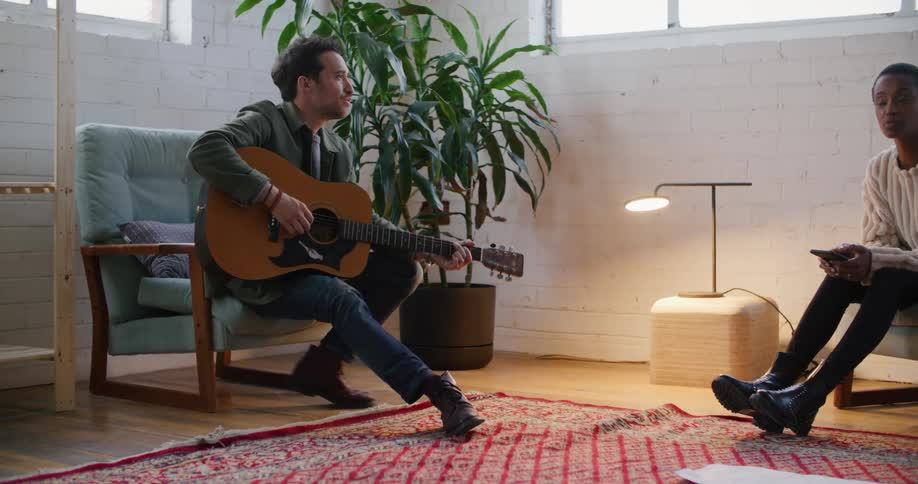 Man playing guitar for a woman sitting in the living room at home
