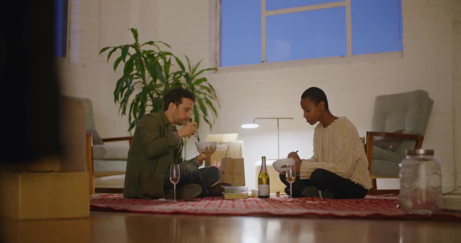 Young couple eating dinner over a blanket on the living room floor at evening