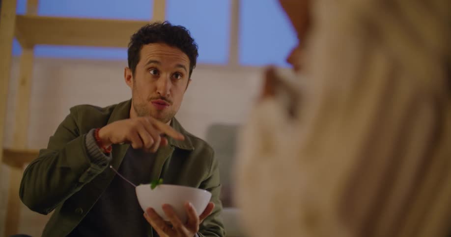 Man eating salad with a friend in the living room at home