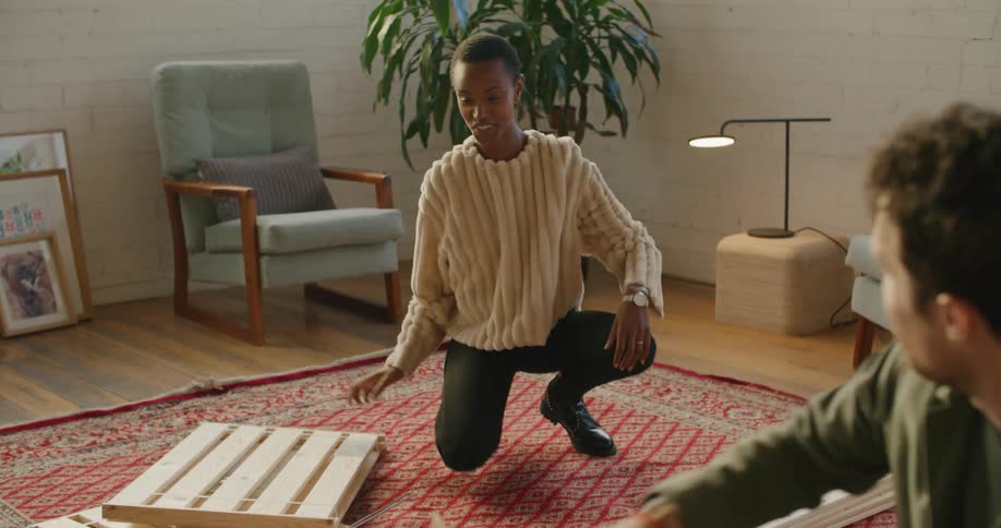 A man and woman unpack boxes and lay out wooden pieces of furniture to be put together
