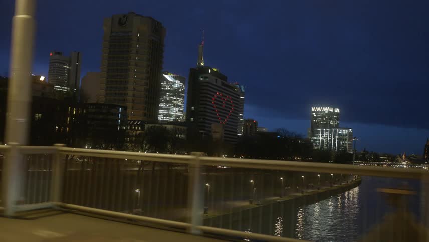 Street lamps lined avenue paralleling water leading to downtown skyscrapers can be seen through bridge rail