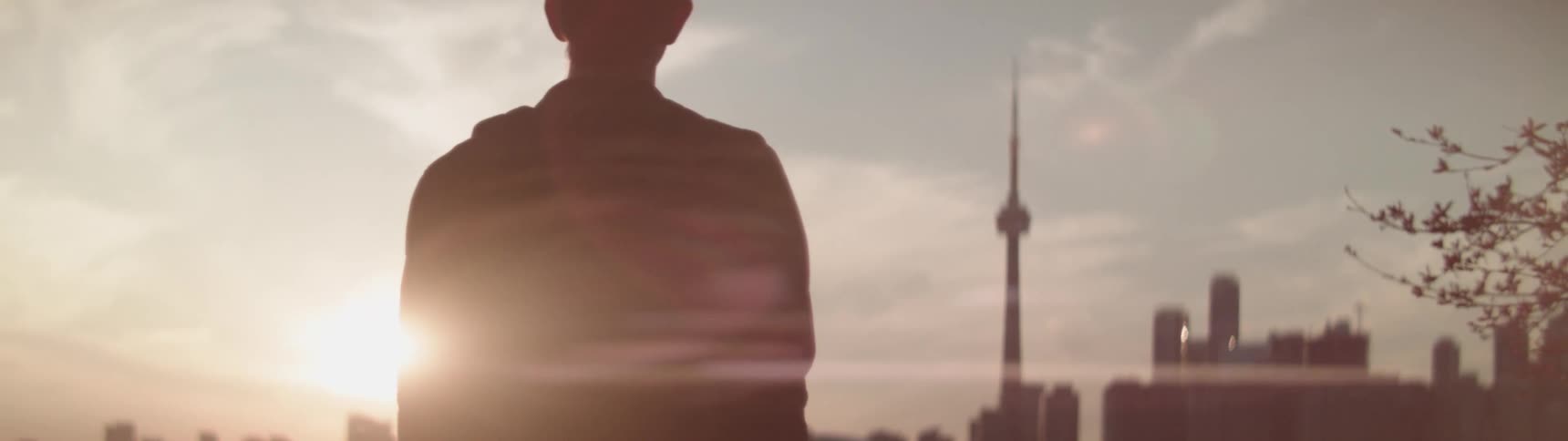 The silhouette of a person standing facing a city skyline with sun glaring